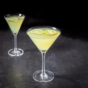 Two glasses with the last word cocktail in them with lime wheels floating - square
