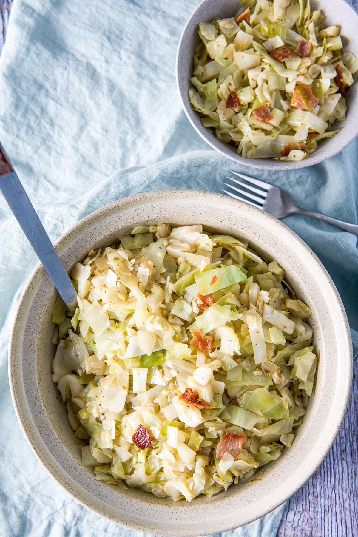 Overhead view of the big and little bowl filled with the cabbage and bacon on a green napkin