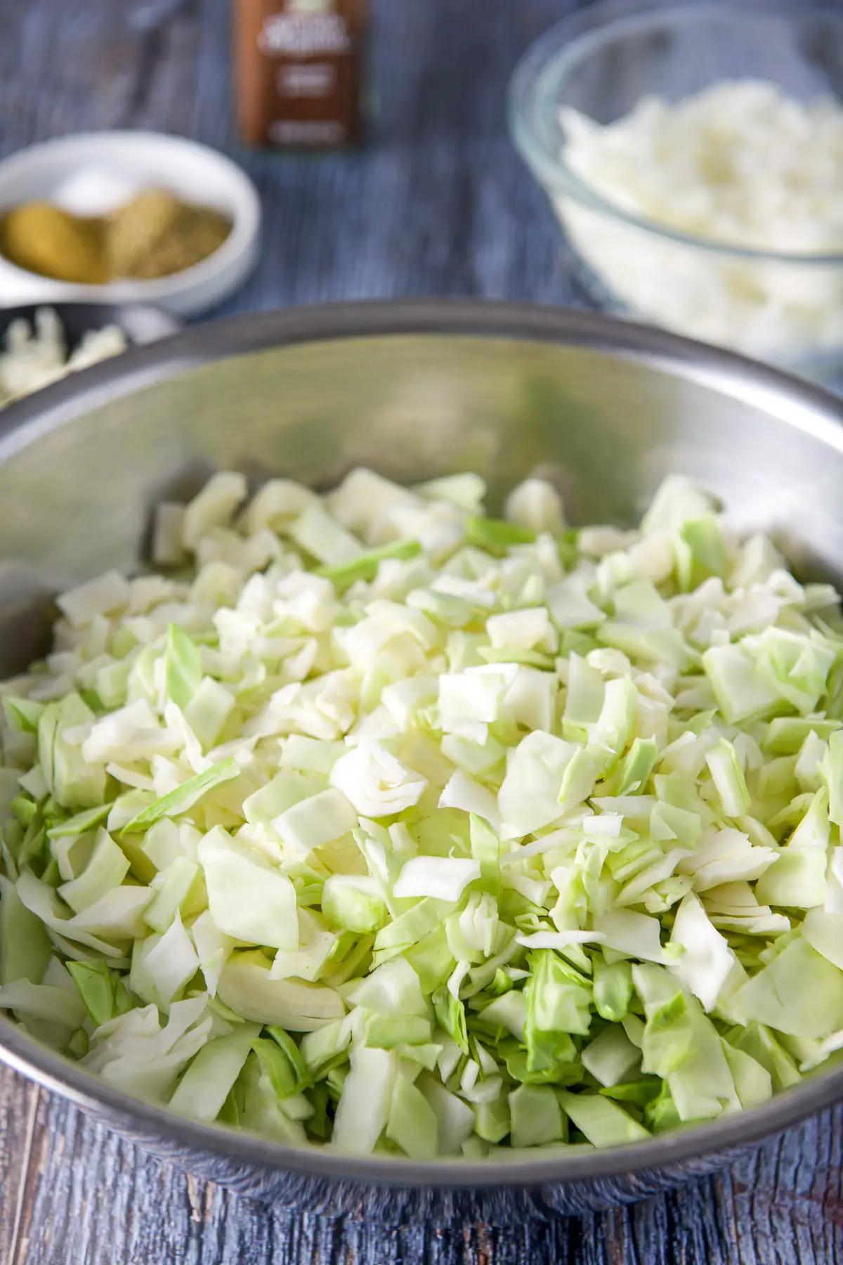 Raw cabbage chopped in a bowl, onions in a bowl and herbs in the back