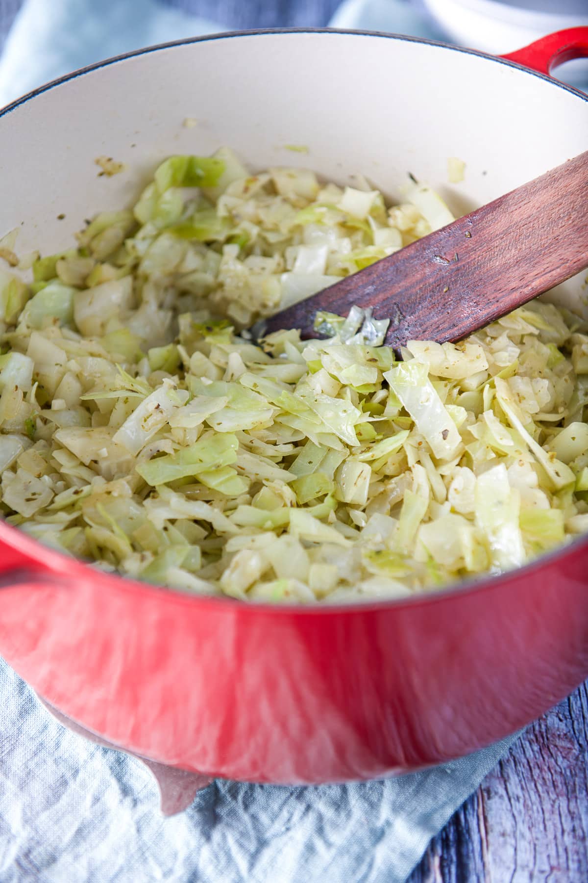 A red Dutch oven with cooked cabbage and a wooden spatula