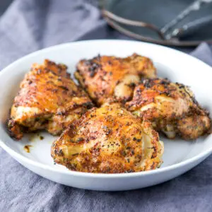 four cooked chicken thighs in a white deep dish - square