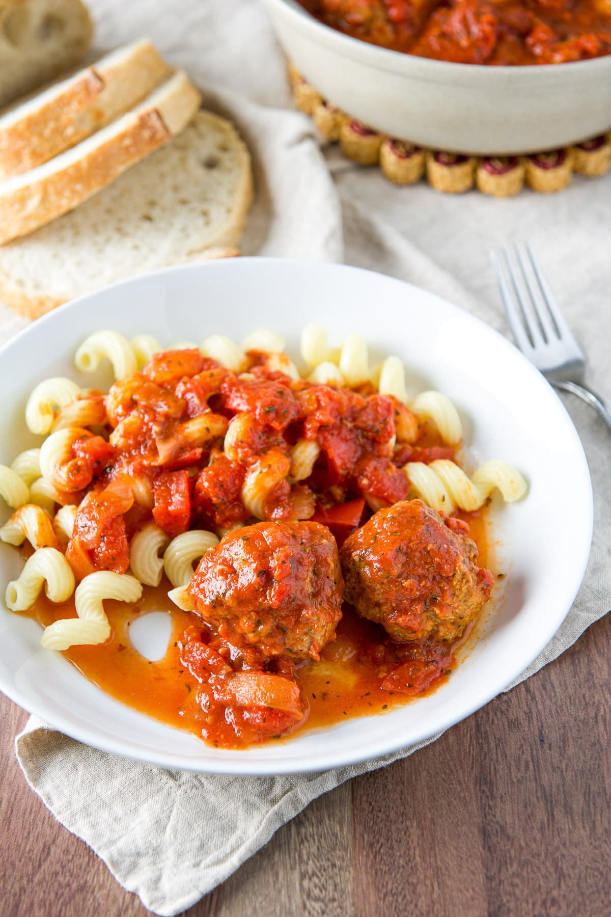 A white deep dish with pasta, sauce and meatballs