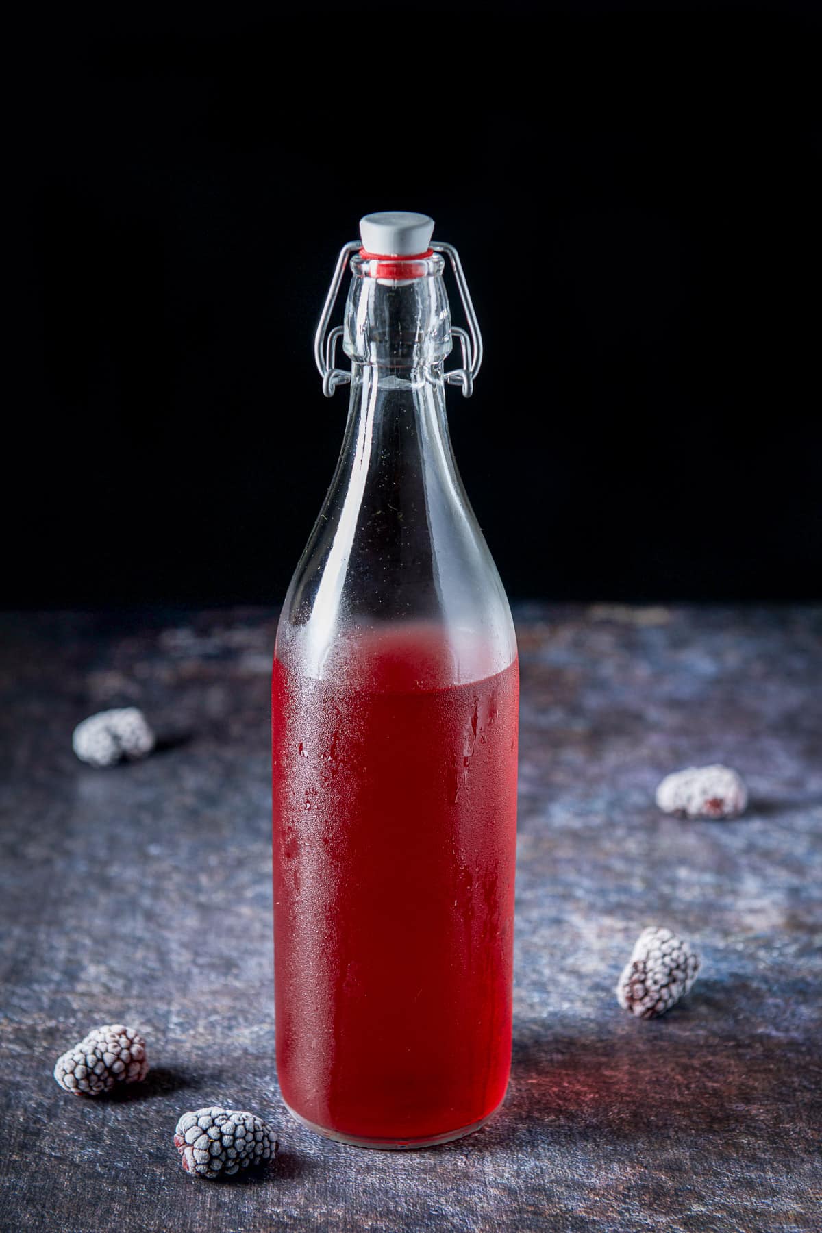 A bottle with a stopper with the infused vodka in it and blackberries on the table