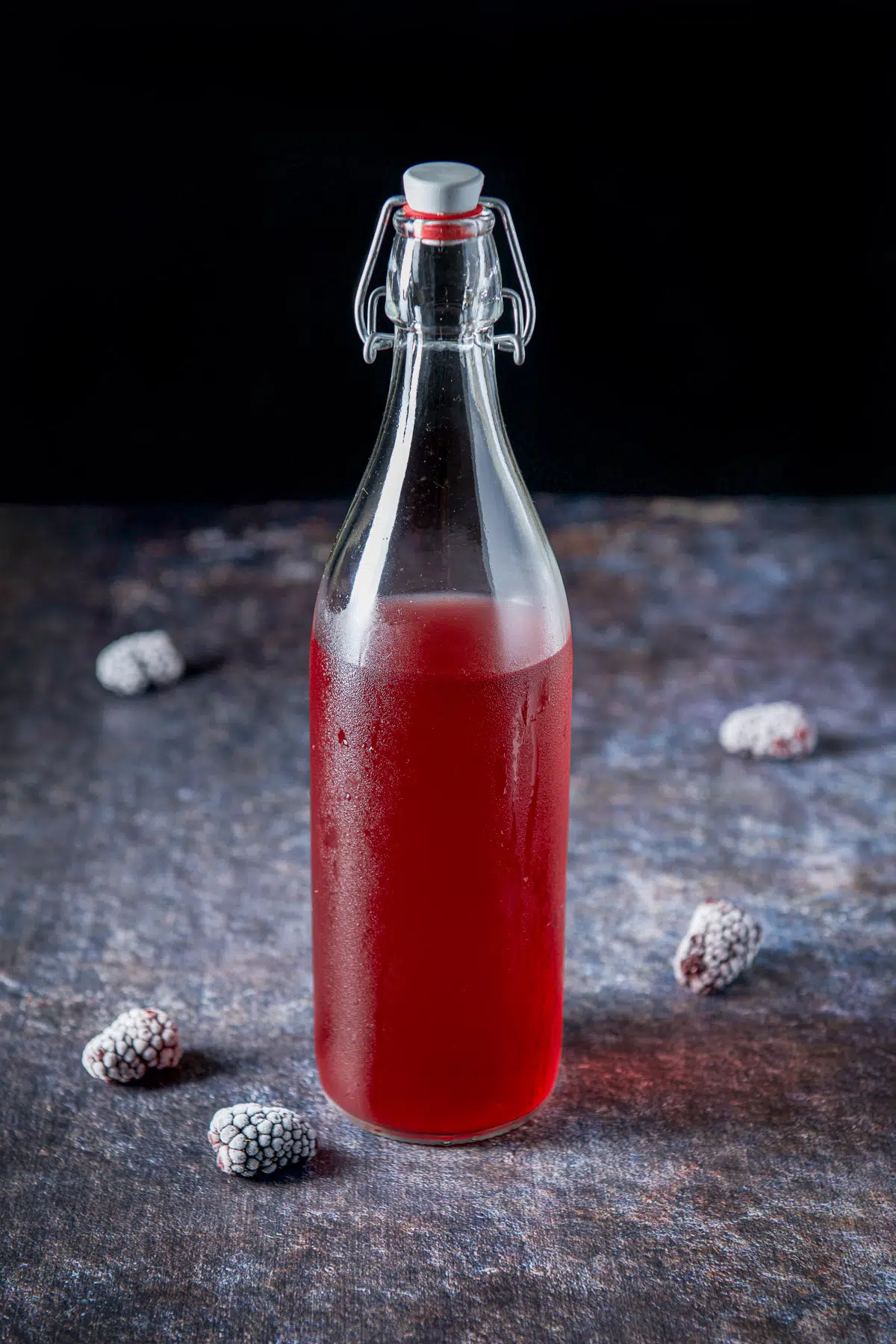 A table with frozen blackberries on it with a bottle of blackberry vodka