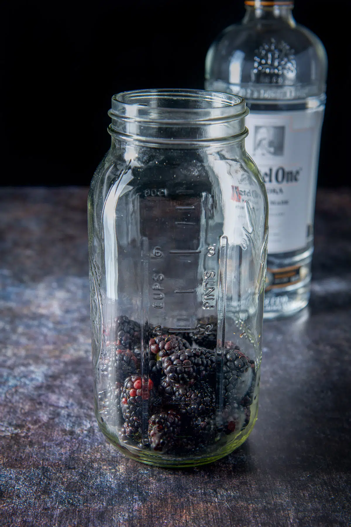 blackberries in a large jar with a bottle of vodka in the background