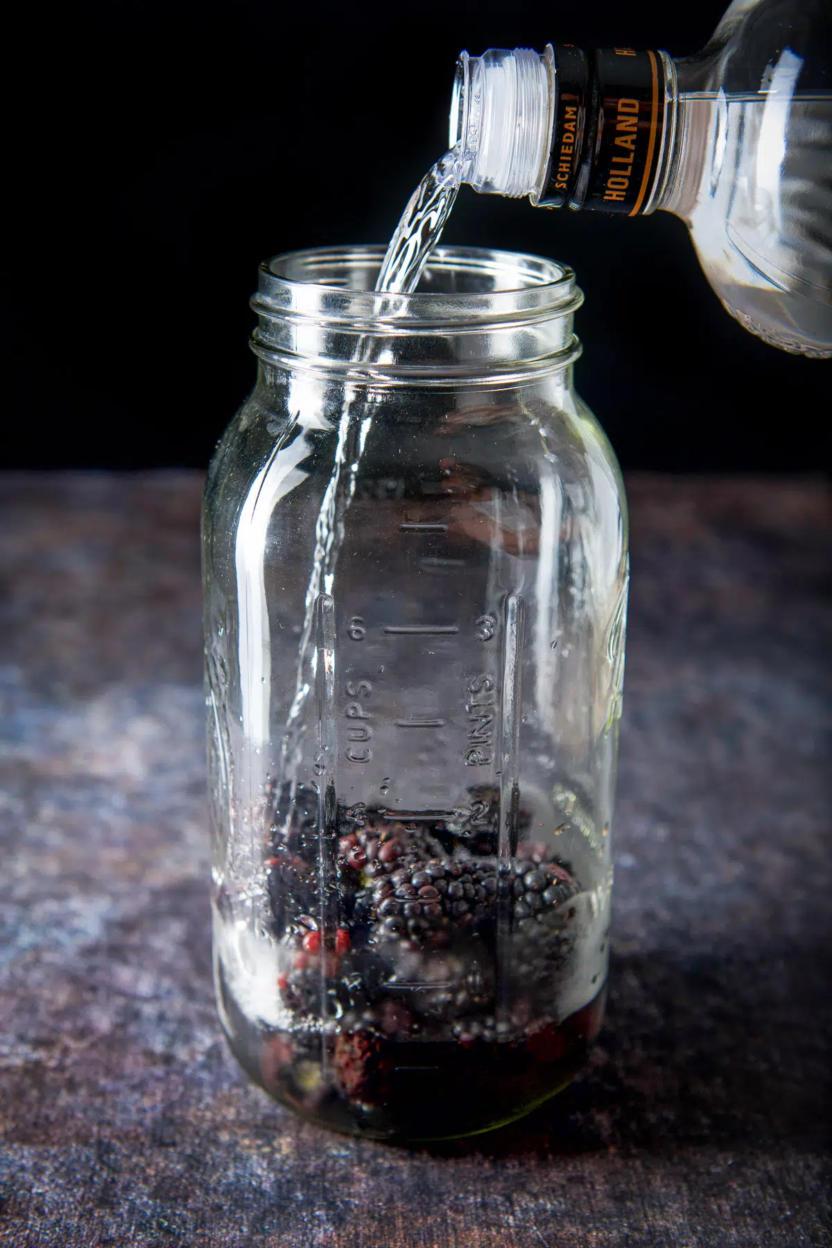 Vodka being poured into the jar of blackberries