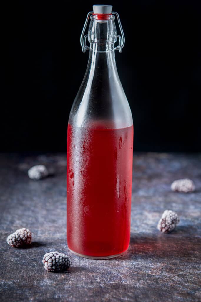 A bottle with the red vodka in it with blackberries on the table