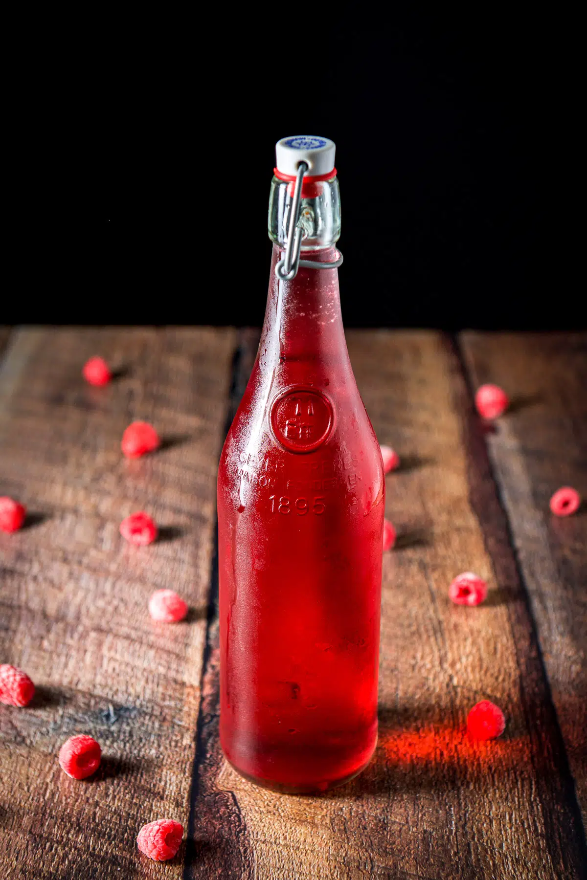 Raspberries on a table with the bottle of red vodka