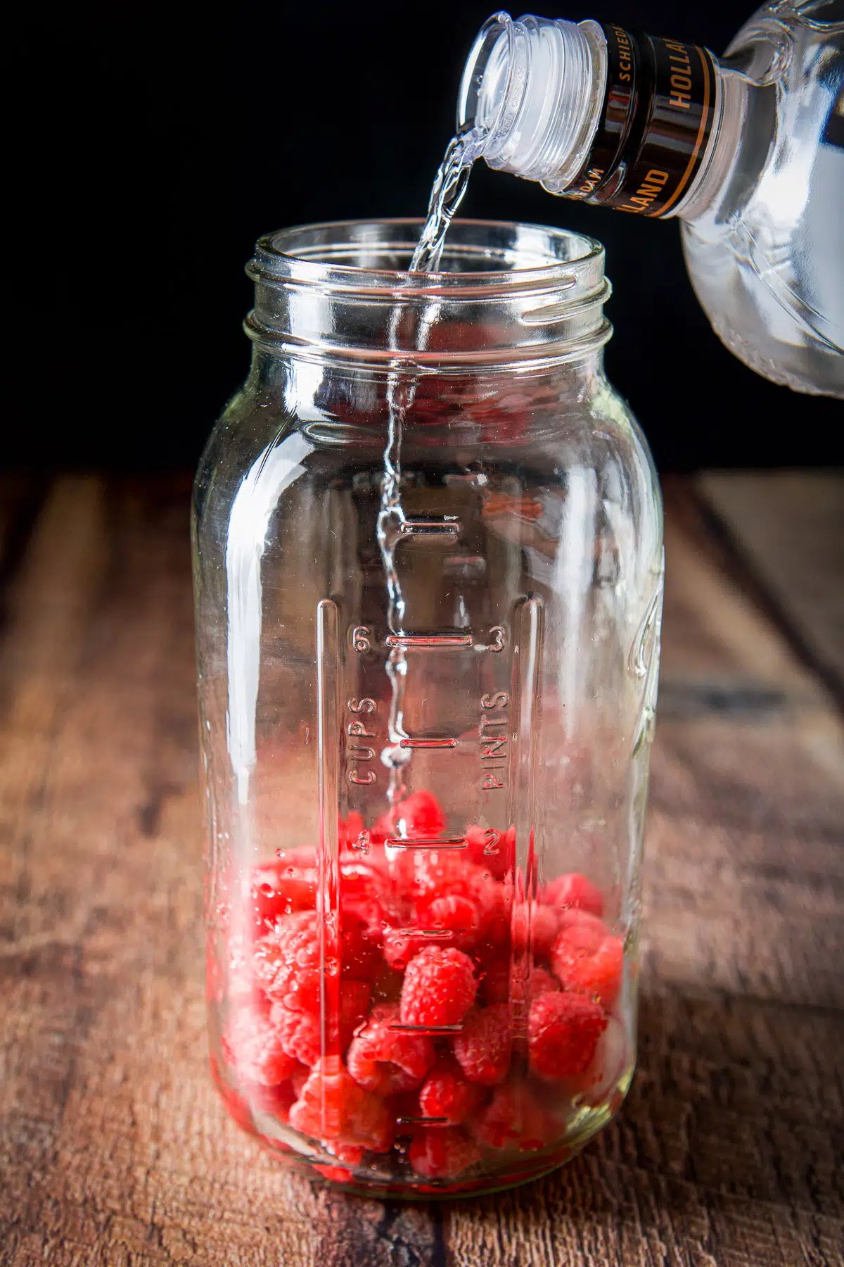 Vodka being poured into the jar over the raspberries
