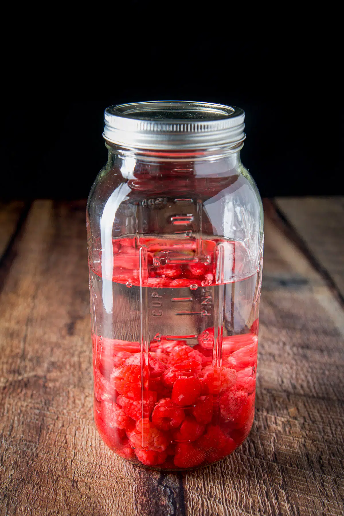 A capped jar with vodka and raspberries in it