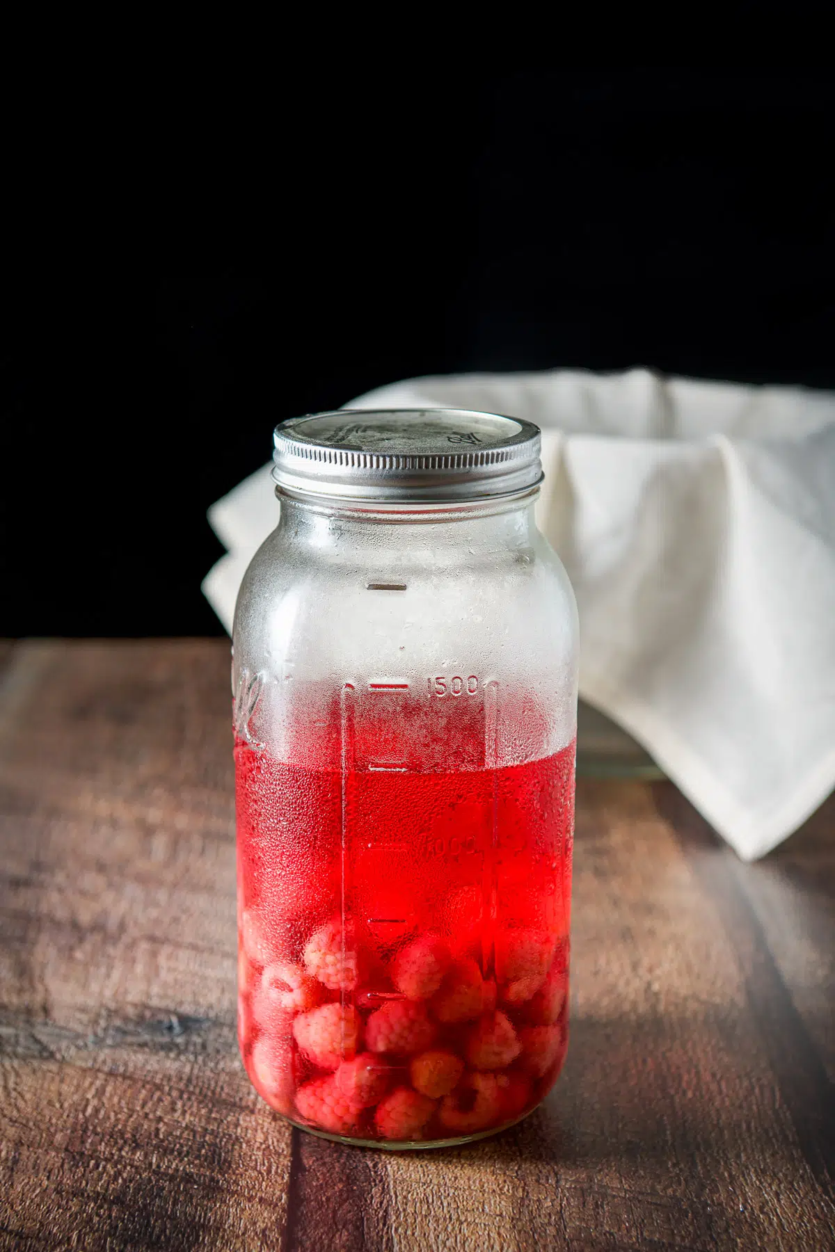 A jar with vodka and raspberries with a sieve in the back