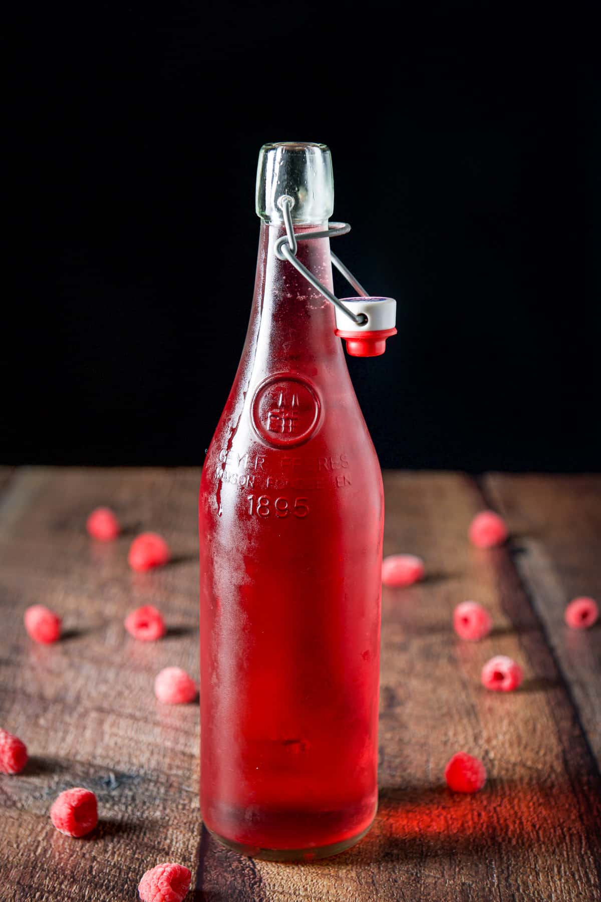 An uncapped bottle with raspberry vodka with raspberries on the table