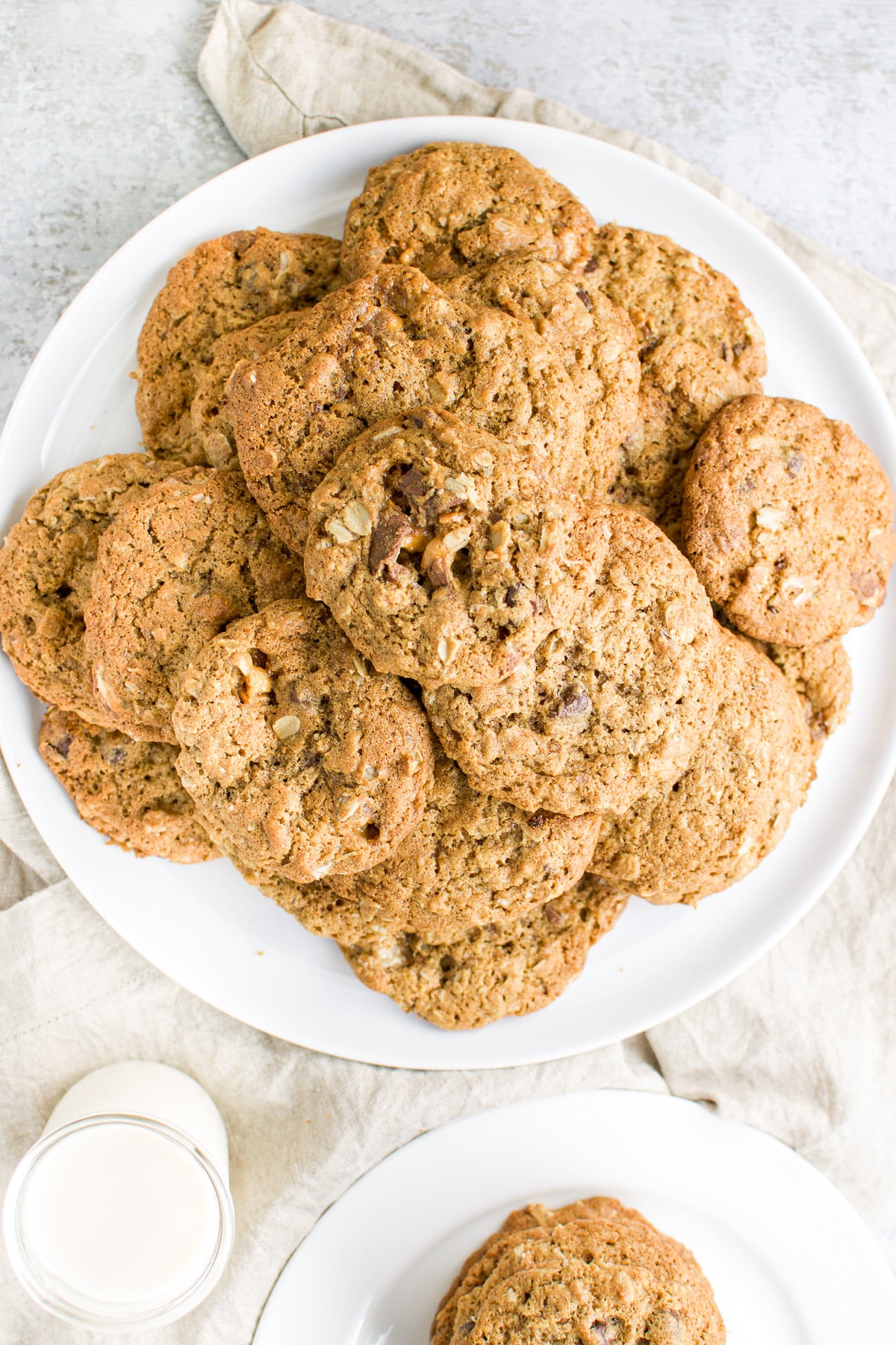 Overhead view of a big plate of cookies along with a glass of milk and small plate