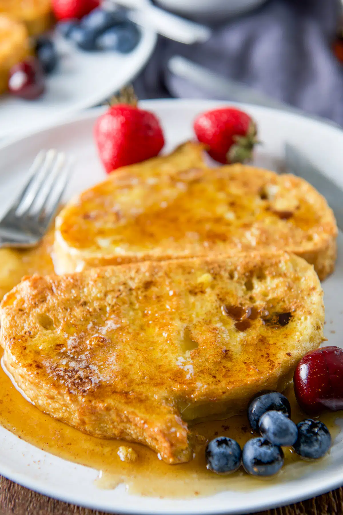 Close up of two pieces of French toast smothered with maple syrup on a plate with fruit