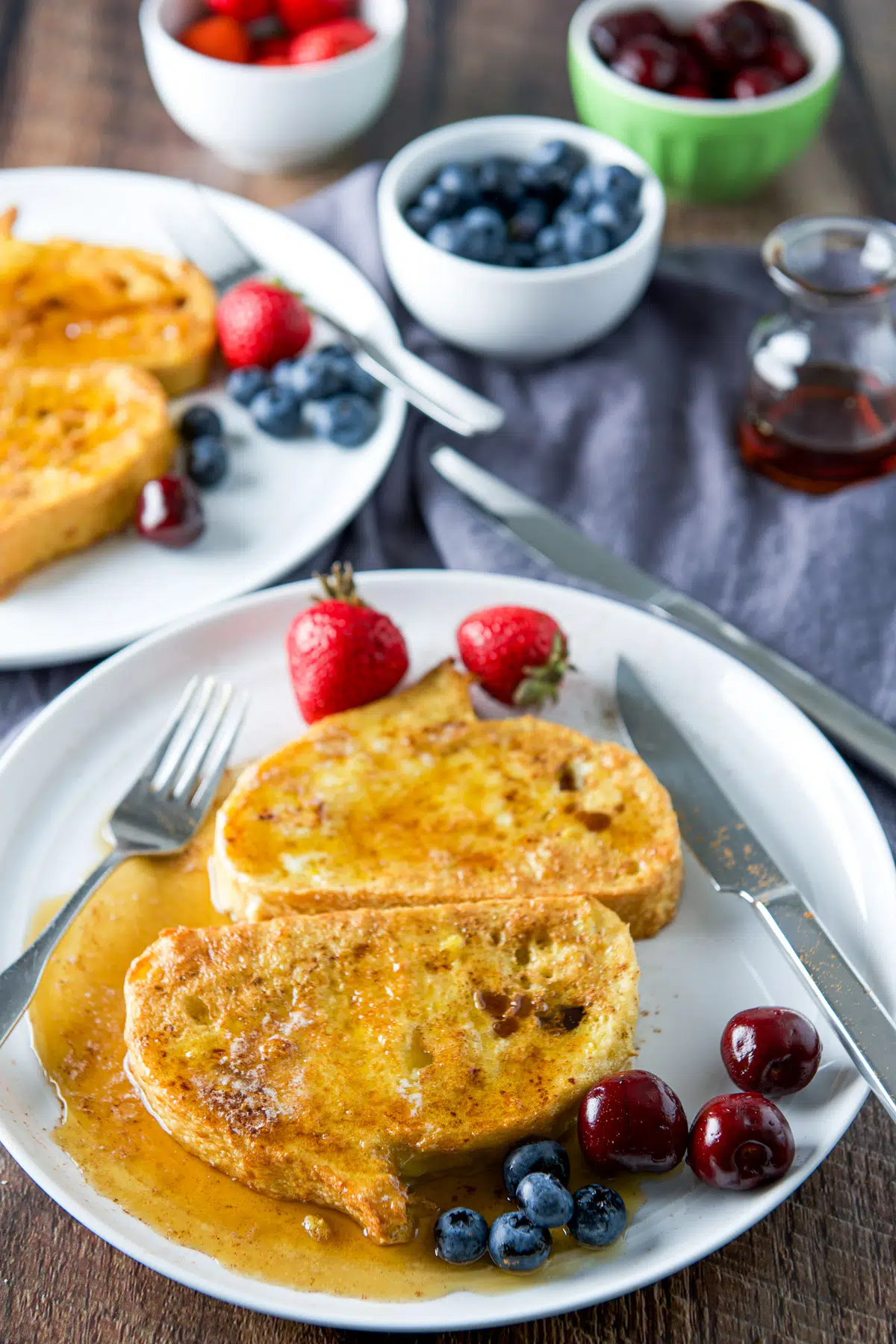 A high view of fruit on plates with French toast that has maple syrup on it