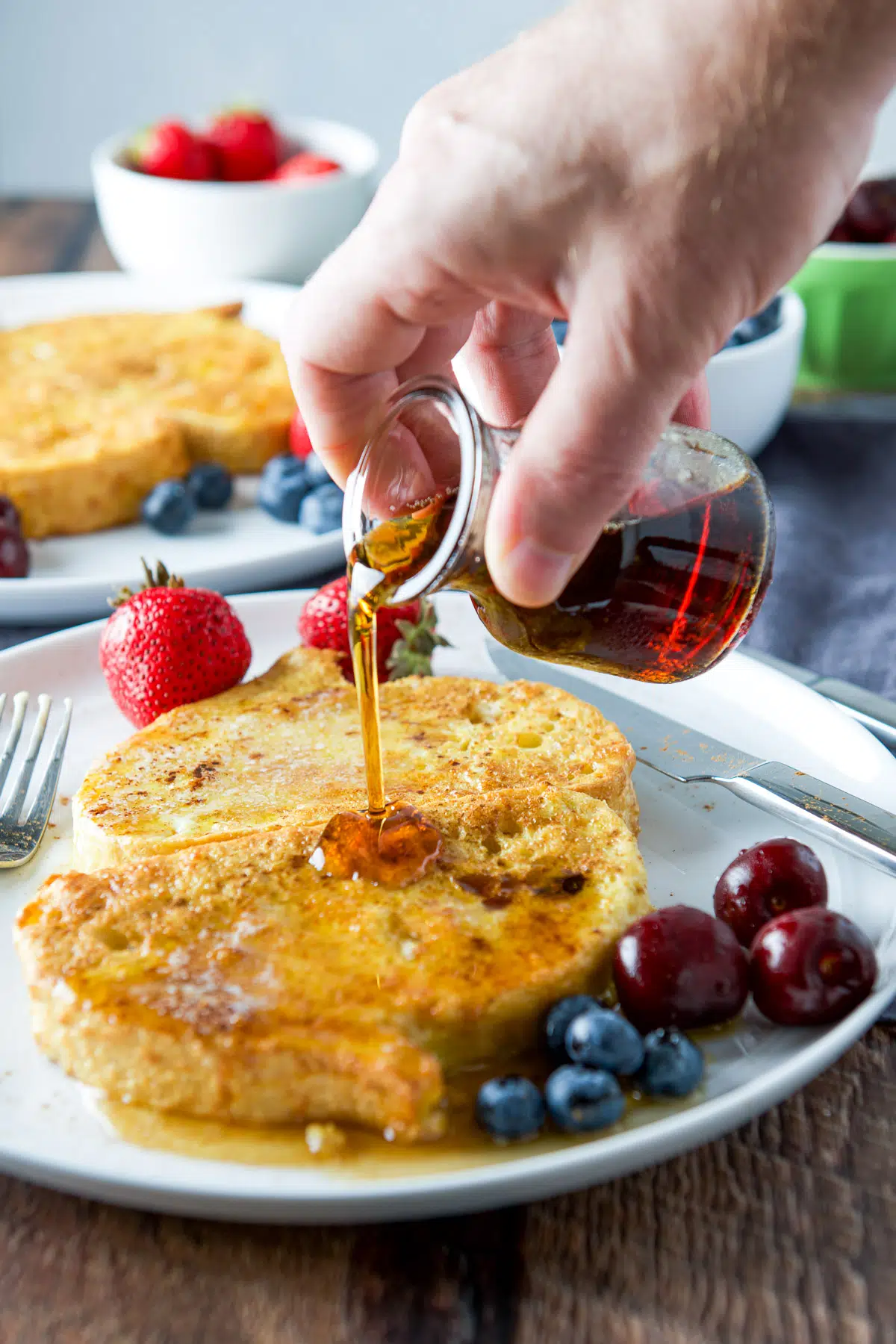 A male hand pouring maple syrup on the buttered French toast
