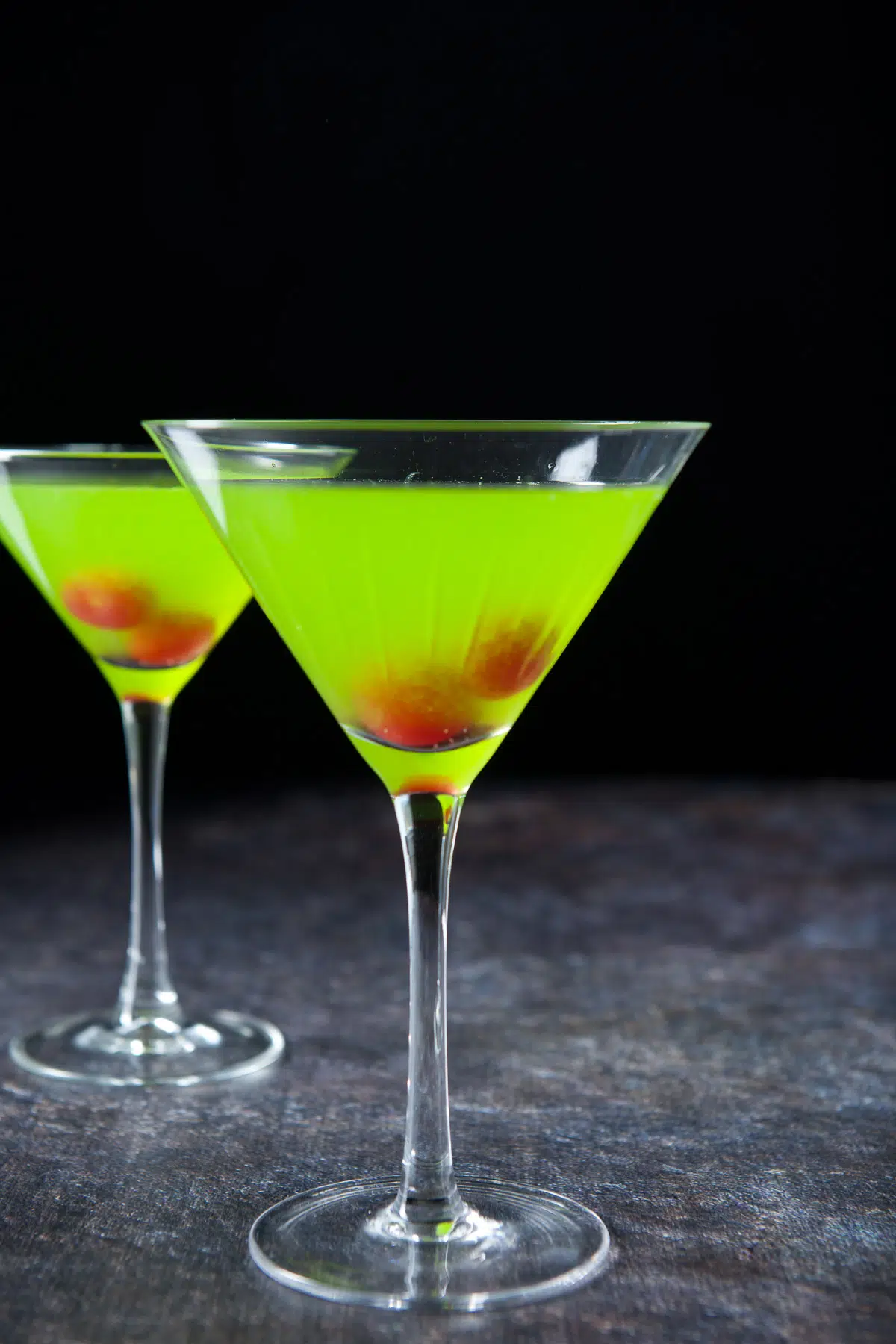 Vertical view of the bright green cocktail with two cherries in each glasses