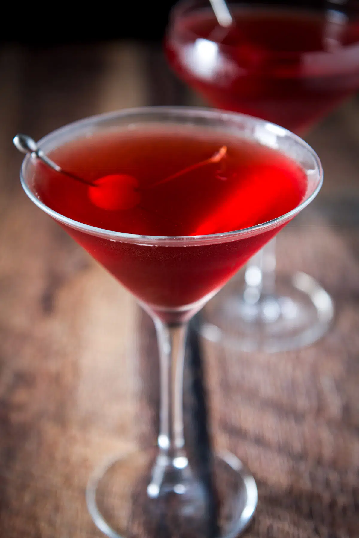 Martini glass with a cherry and pick in it filled with the red drink