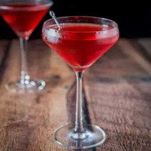 Curved glass with the red cocktail in it in front of a martini glass
