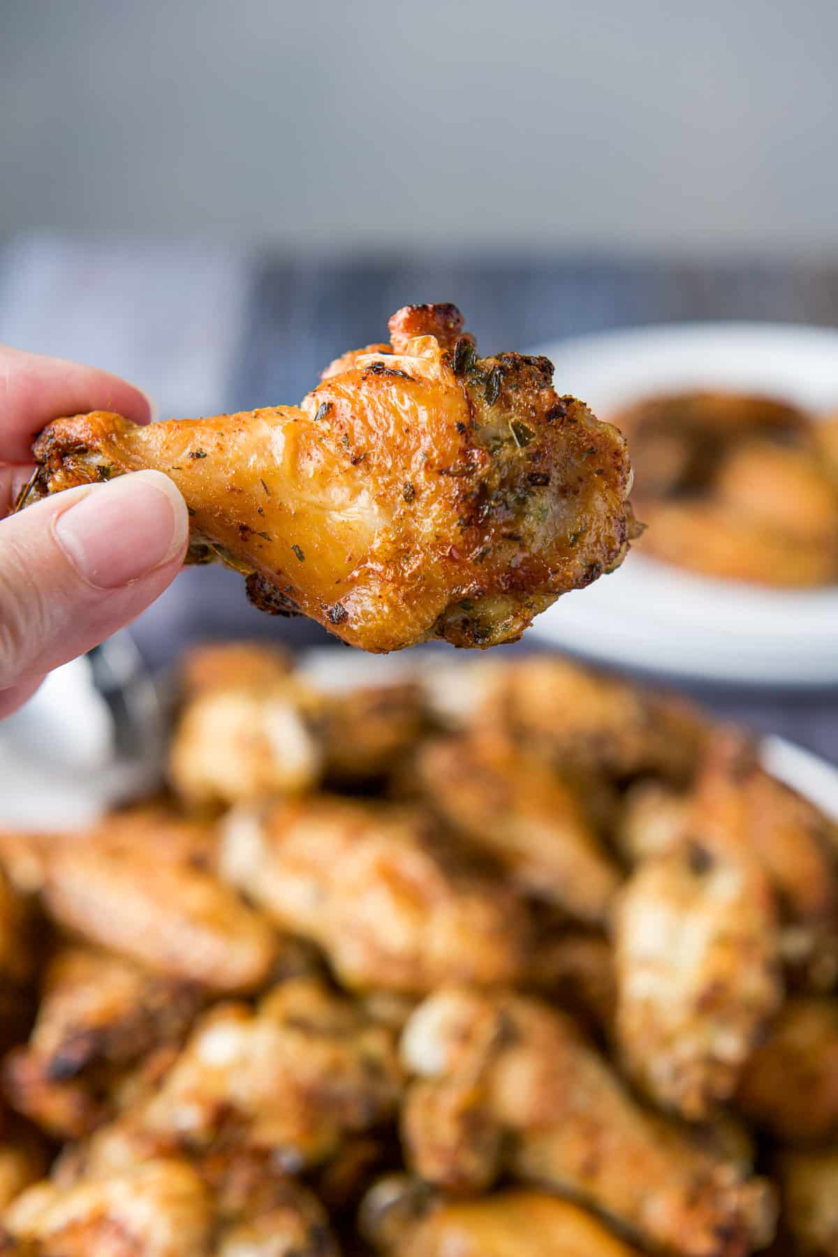 A hand holding a wing drumette over a plater of wings