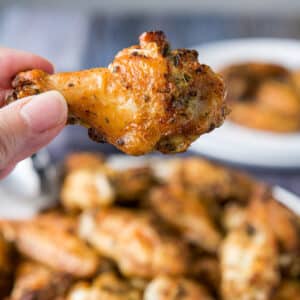 A hand holding a wing drummie over a platter of them