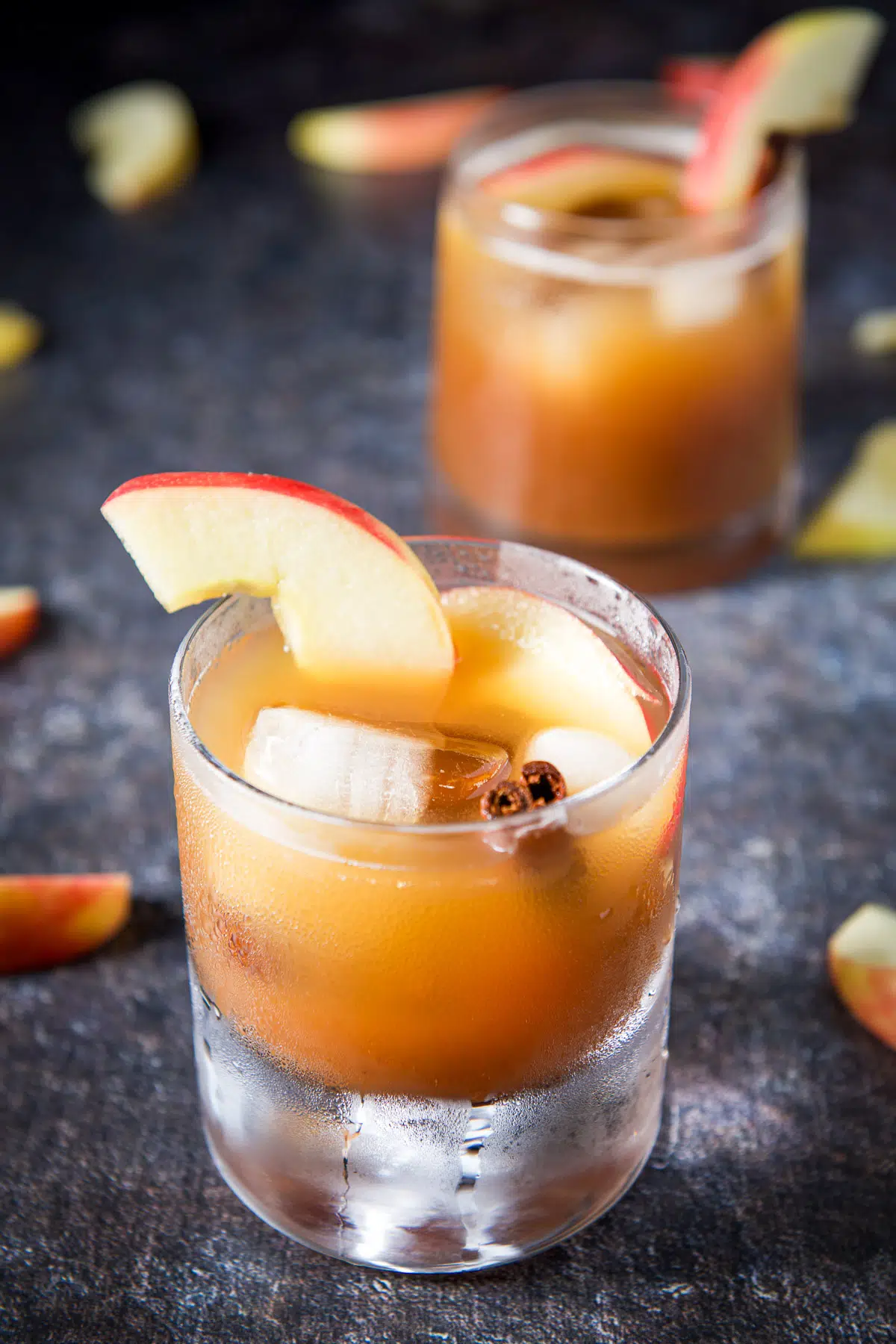 A thick bottom glass filled with the old fashioned with a cinnamon stick and apple slices