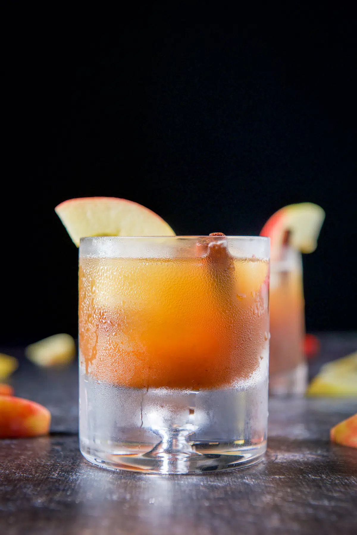 Vertical view of the heavy bottomed glass with the apple cocktail with apple slices and cinnamon stick