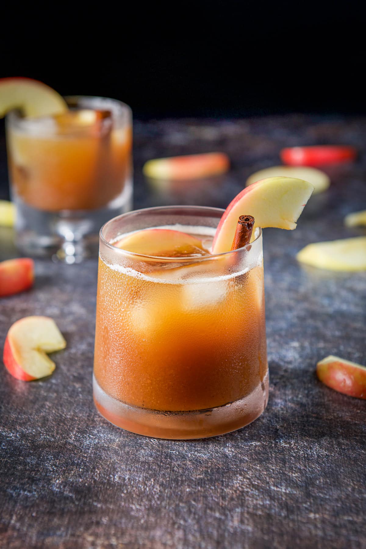 A bunch of apple slices on a table with two apple drinks