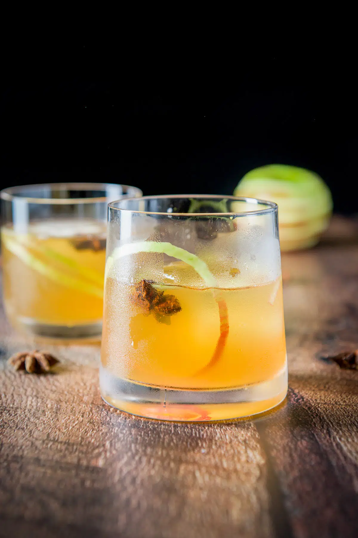 Vertical view of the apple cocktail in glasses with apple skin twist and star anise