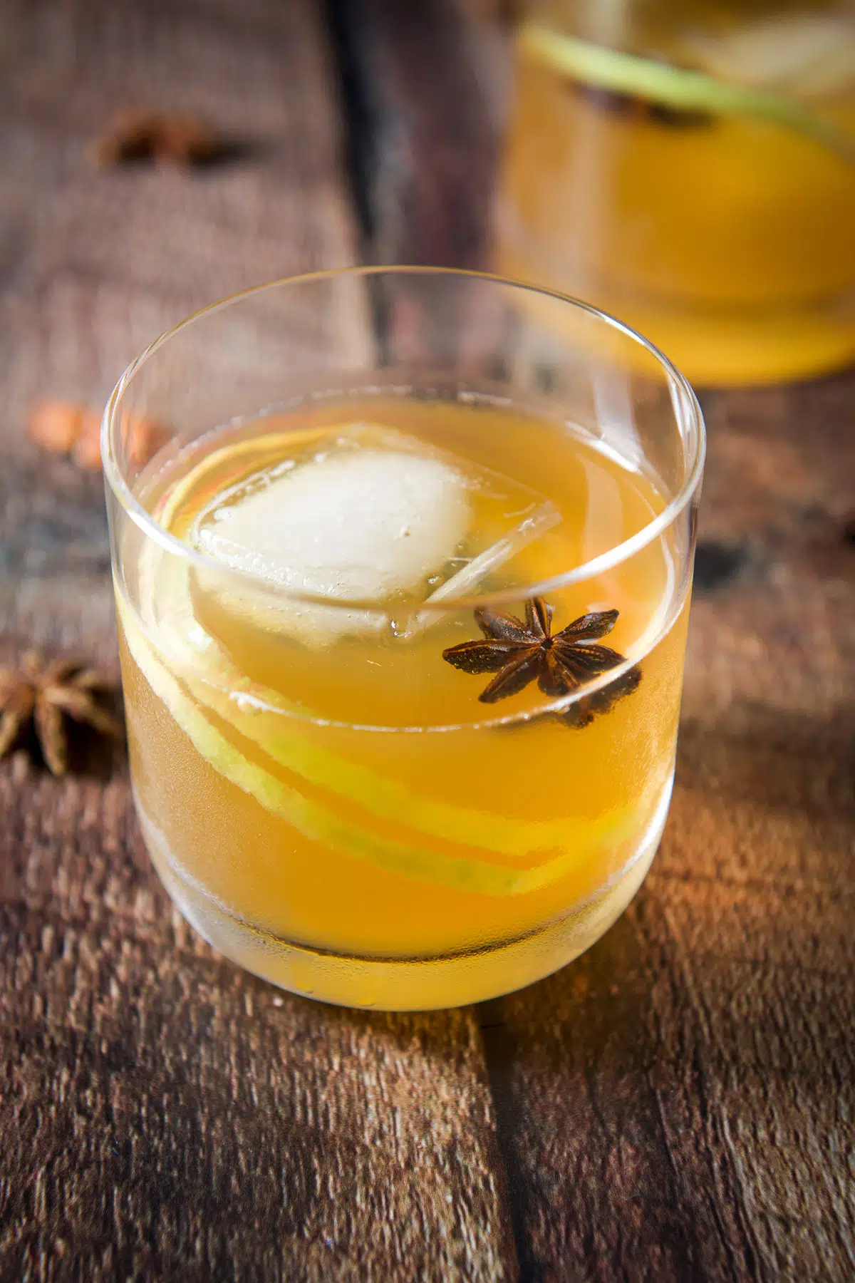 A double old fashioned glass with the amber cocktail in it with a star anise floating