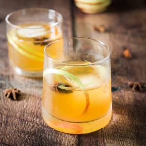 Two old fashioned glasses filled with an apple cocktail with star anise and apple twist in it