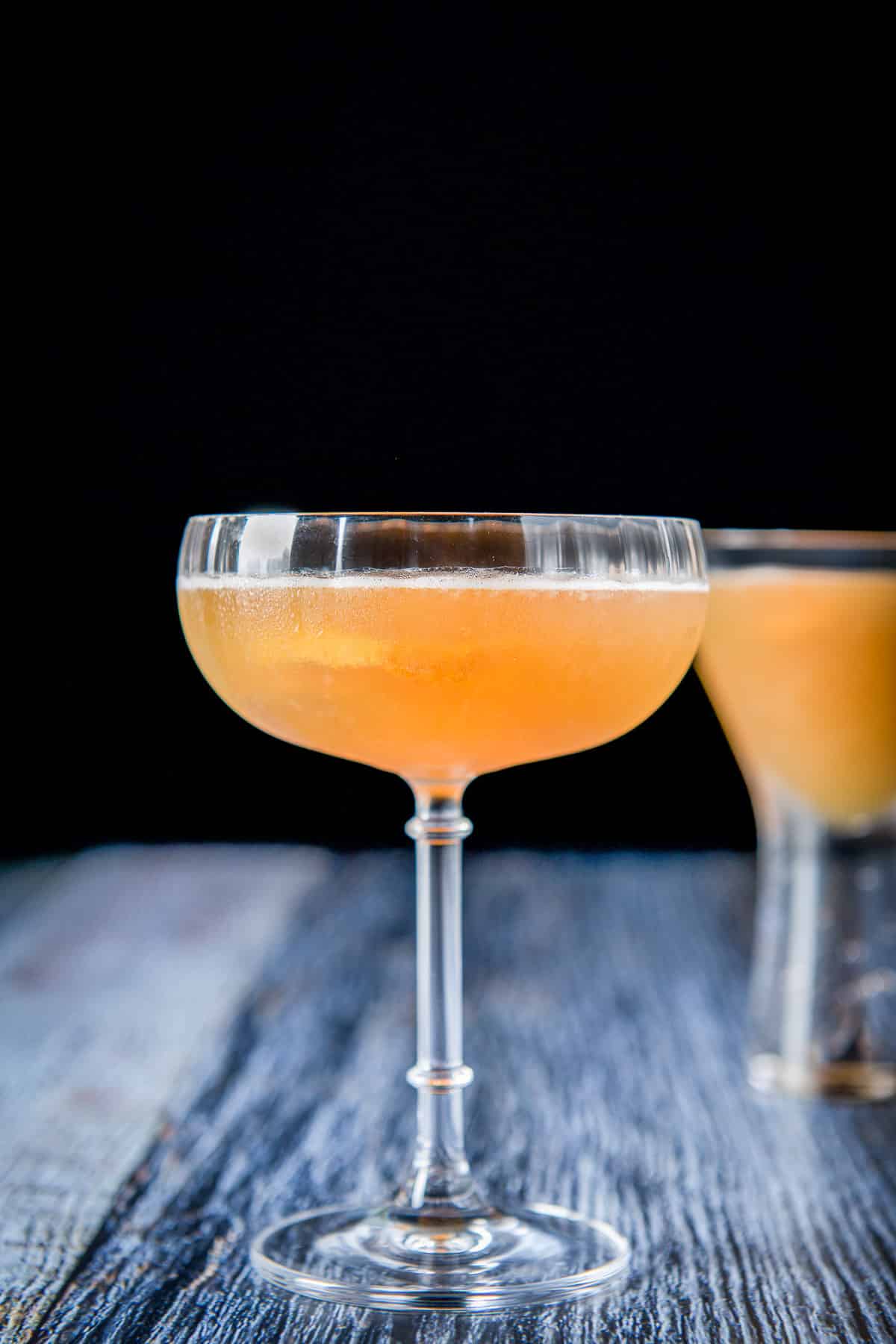 Fluted glass with the orange drink in it with a twist in it