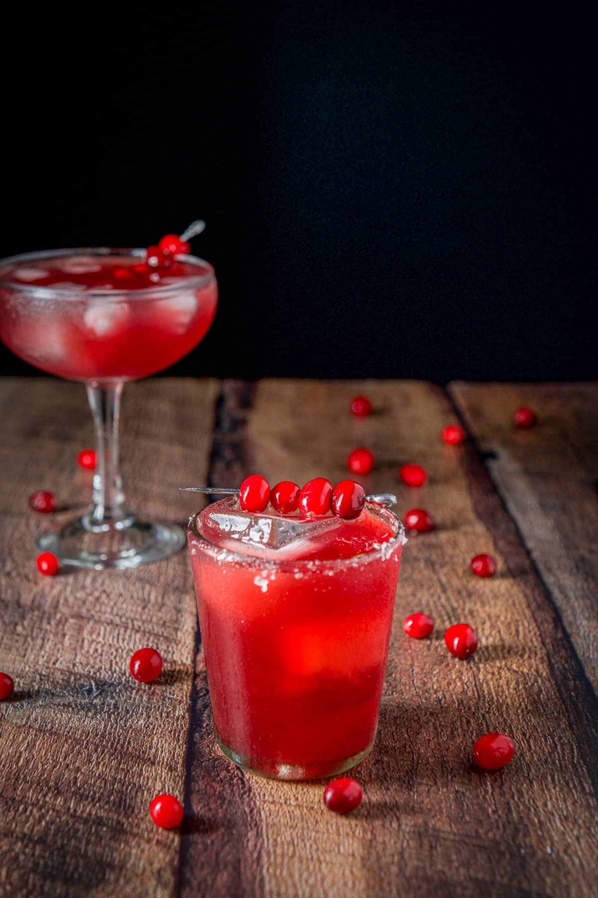 The short glass with salt on the rim filled with the margarita with cranberries on the table