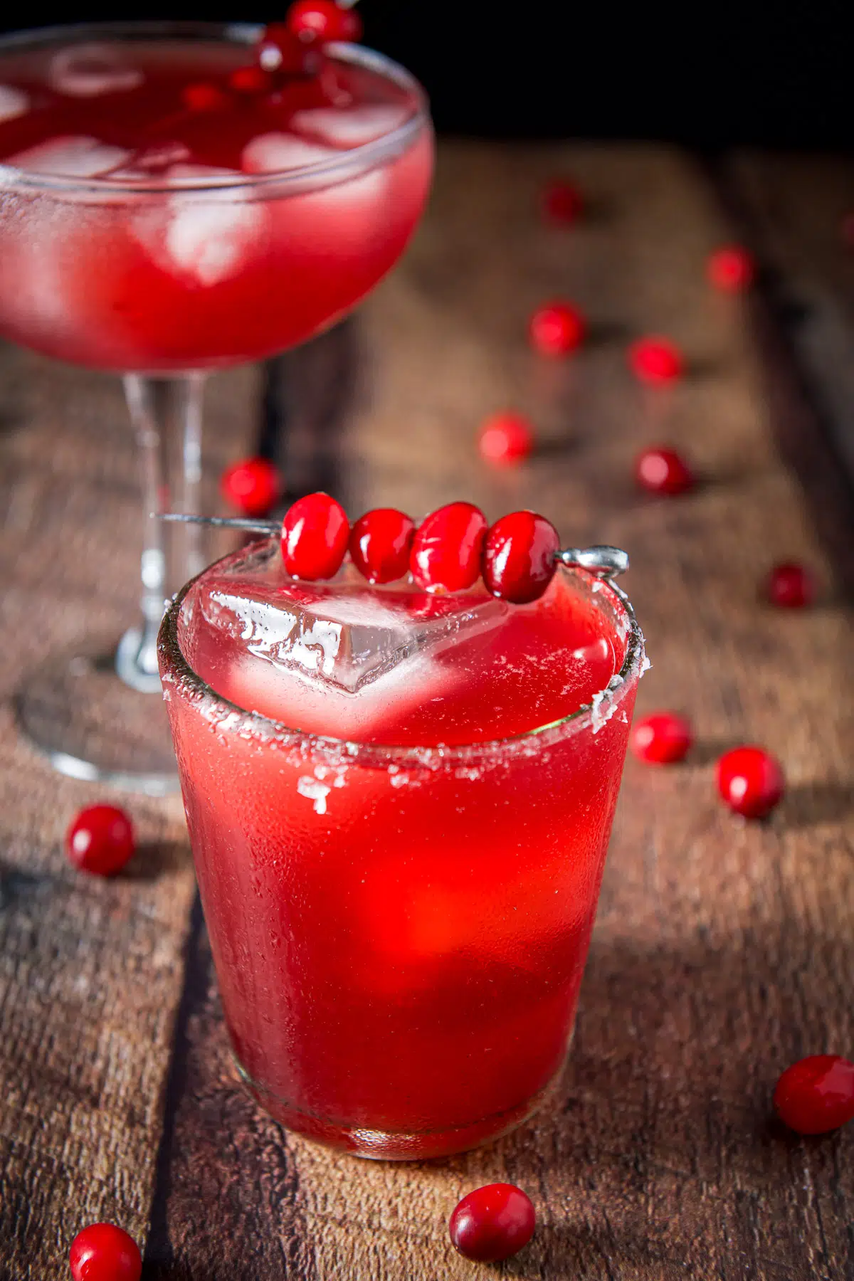 Close up of the cranberry cocktail with a spear of cranberries as garnish and the bowl glass in the background