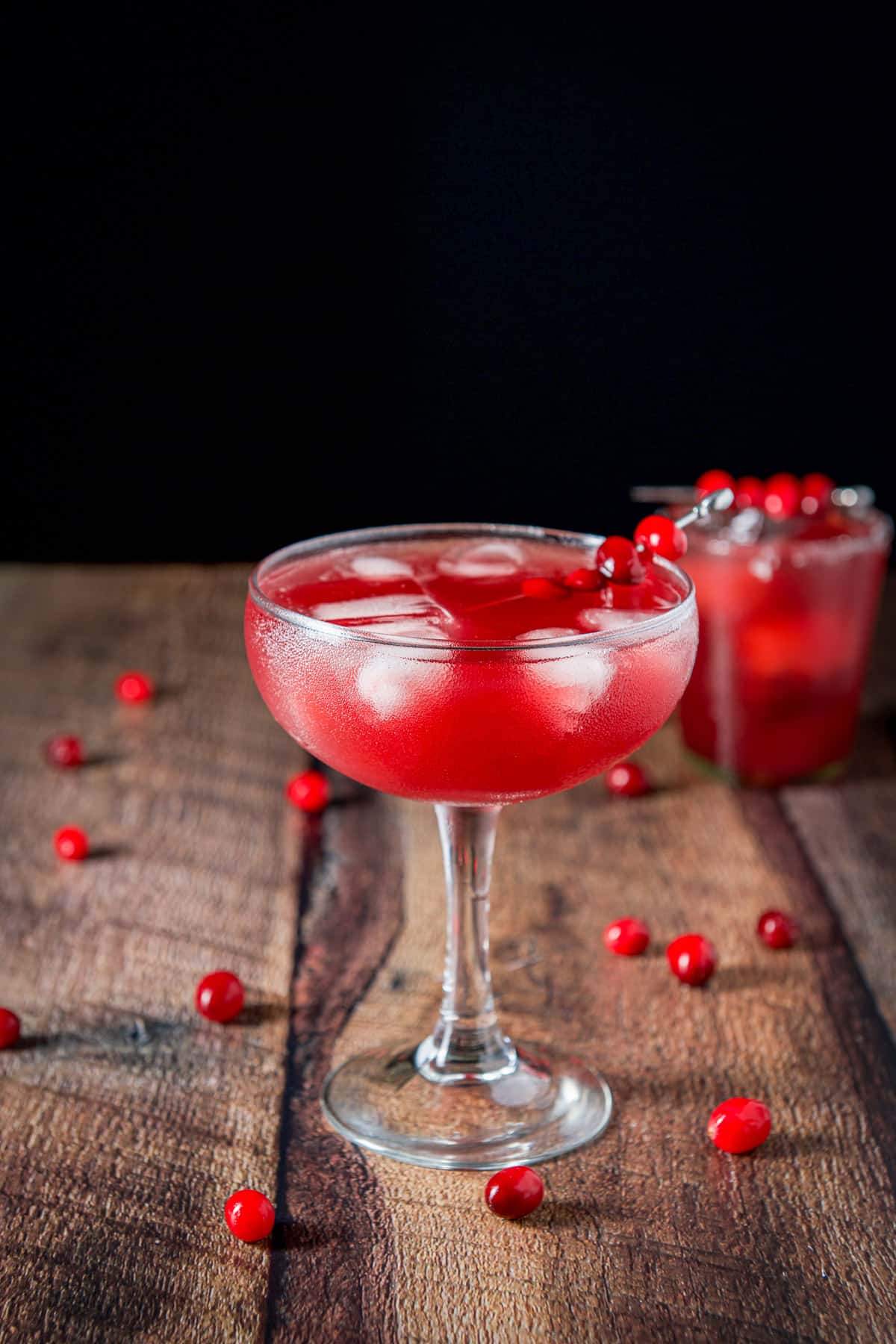 The big glass of red margarita in front of the shorter glass with cranberries on the table