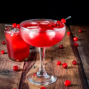 A wide margarita glass filled with the cranberry drink with cranberries on the table