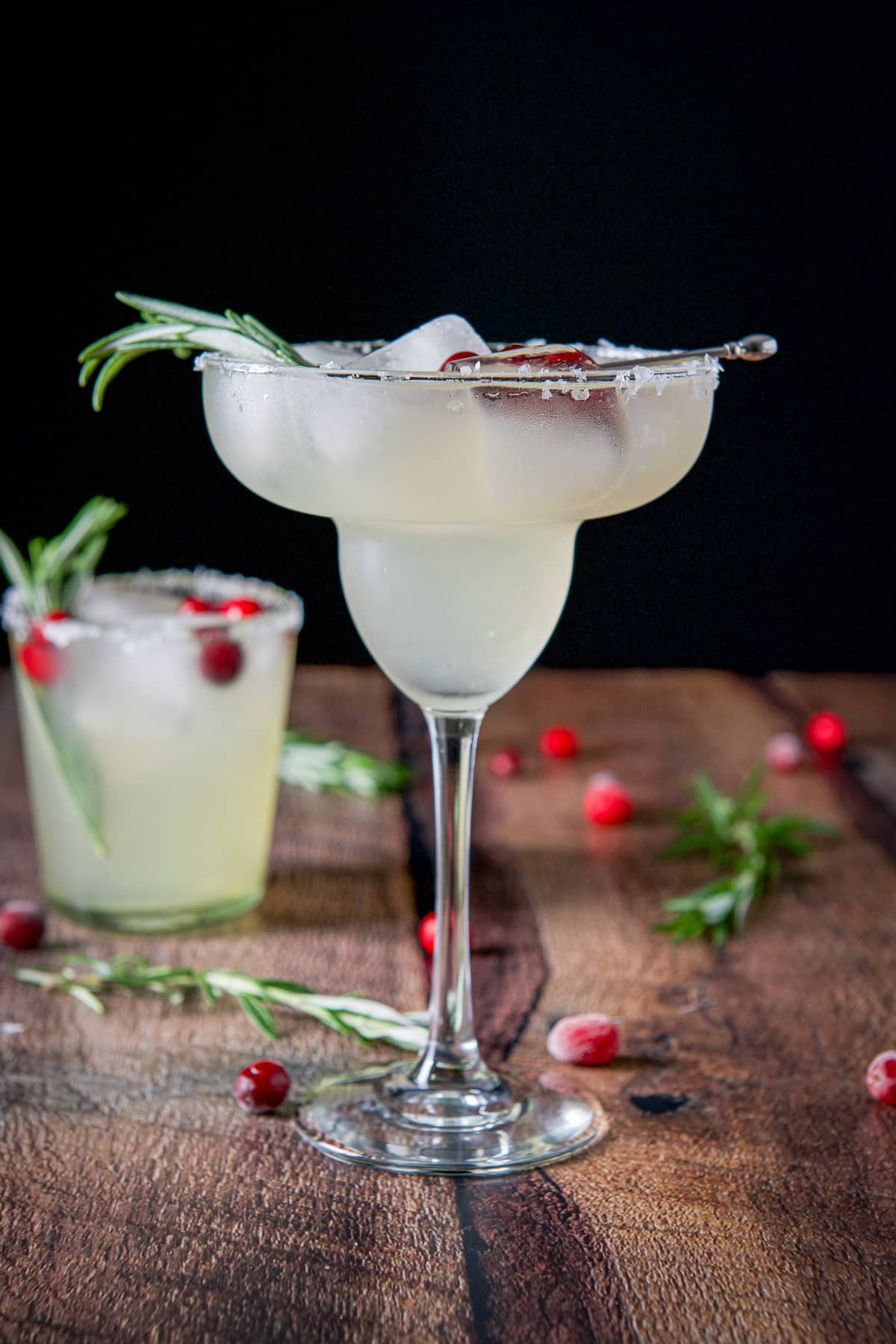 Vertical view of the classic margarita glass with the drink it it with cranberries and rosemary sprigs