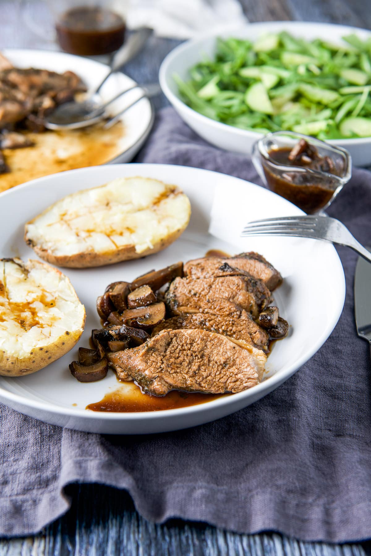 A white deep dish with slices of pork, mushrooms, marinade and baked potato