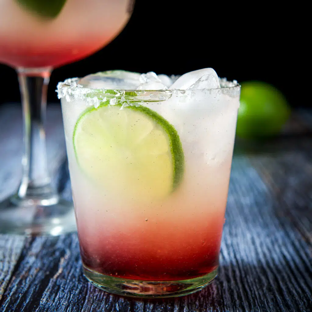 A double old fashioned glass with the layered margarita with a lime wheel as garnish