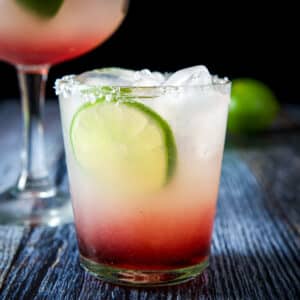 A double old fashioned glass with the layered margarita with a lime wheel as garnish