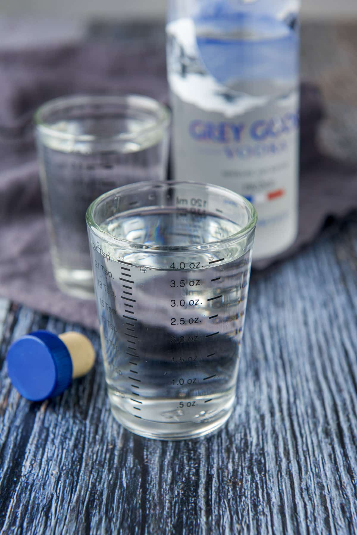Two measuring glasses filled with vodka with the bottle in the back