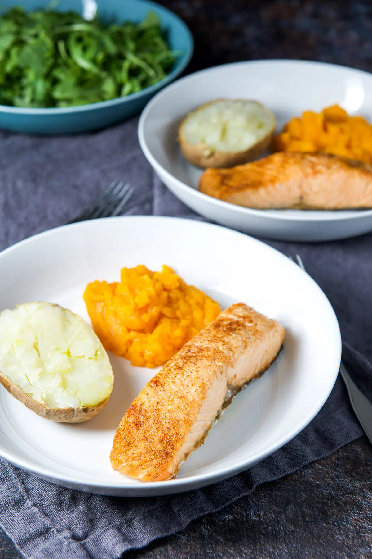 two plates with salmon with potato, squash and a salad in the back