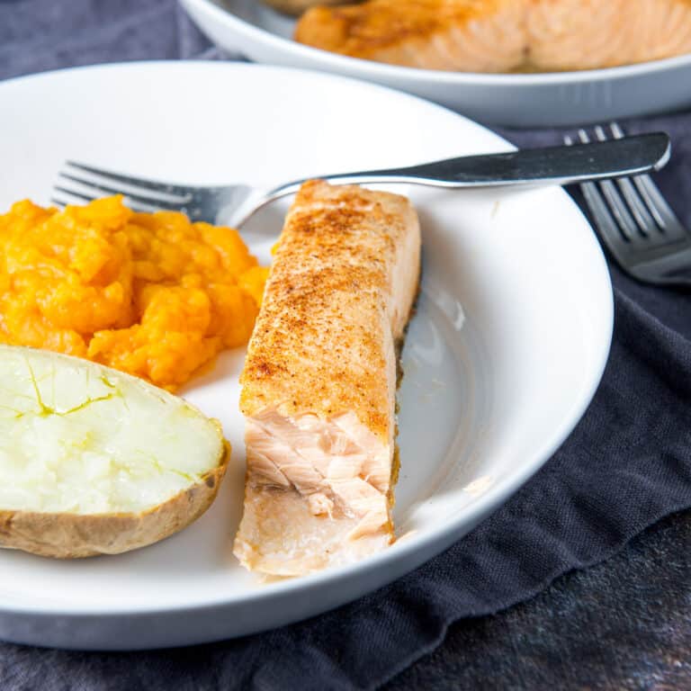 A chunk missing from salmon on a plate with potato and squash - square