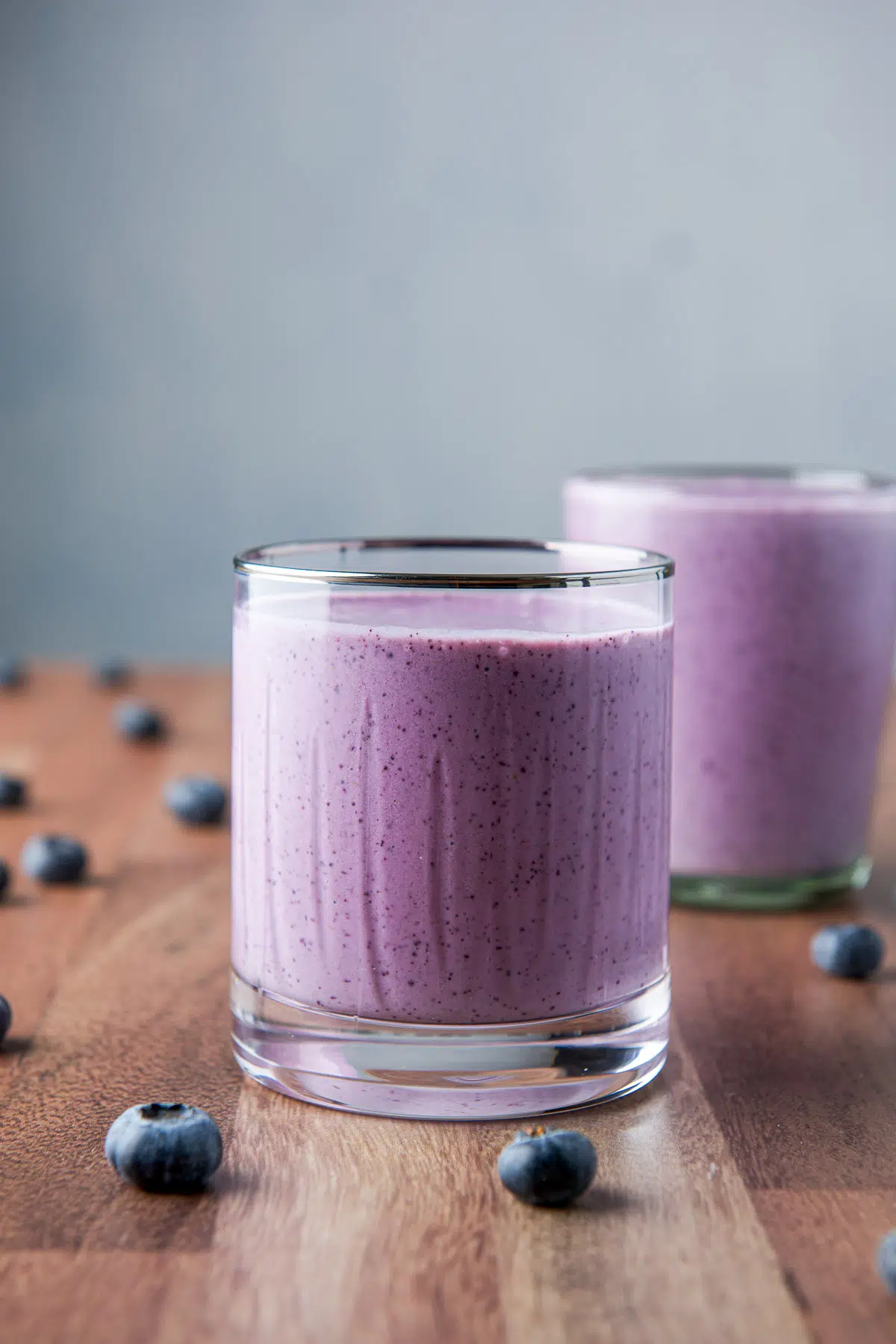 Vertical view of the ridged, silver rimmed glass filled with the blue smoothie with blueberries on the table