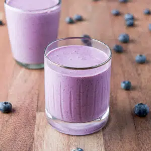 two glasses filled with the blueberry smoothie with blueberries on the wood table