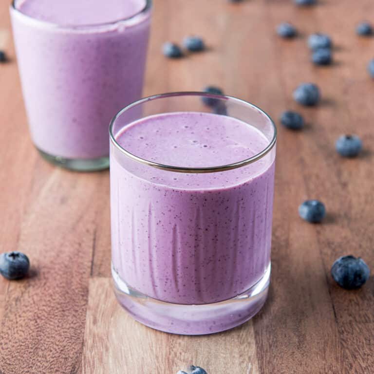 two glasses filled with the blueberry smoothie with blueberries on the wood table