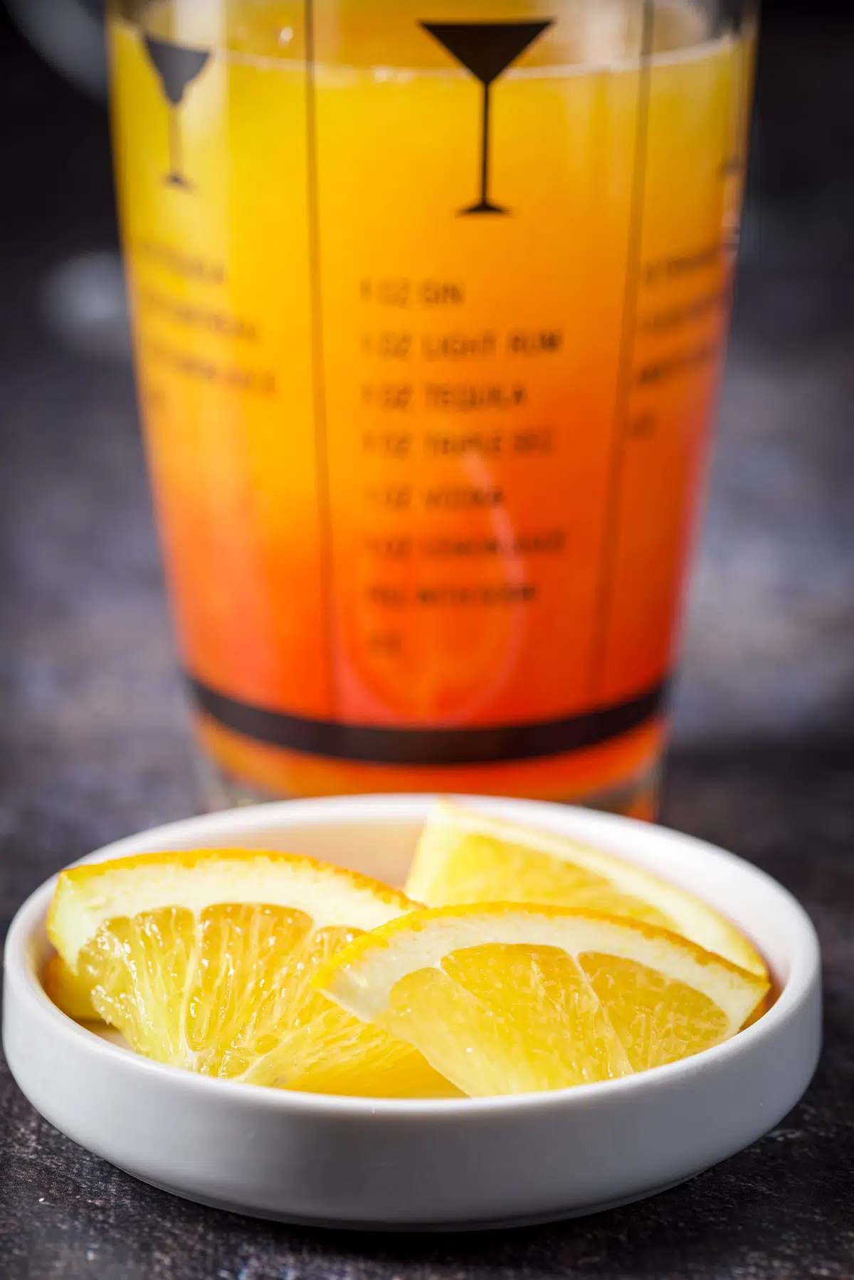 Orange slices in a white bowl with the cocktail shaker filled with the hurricane