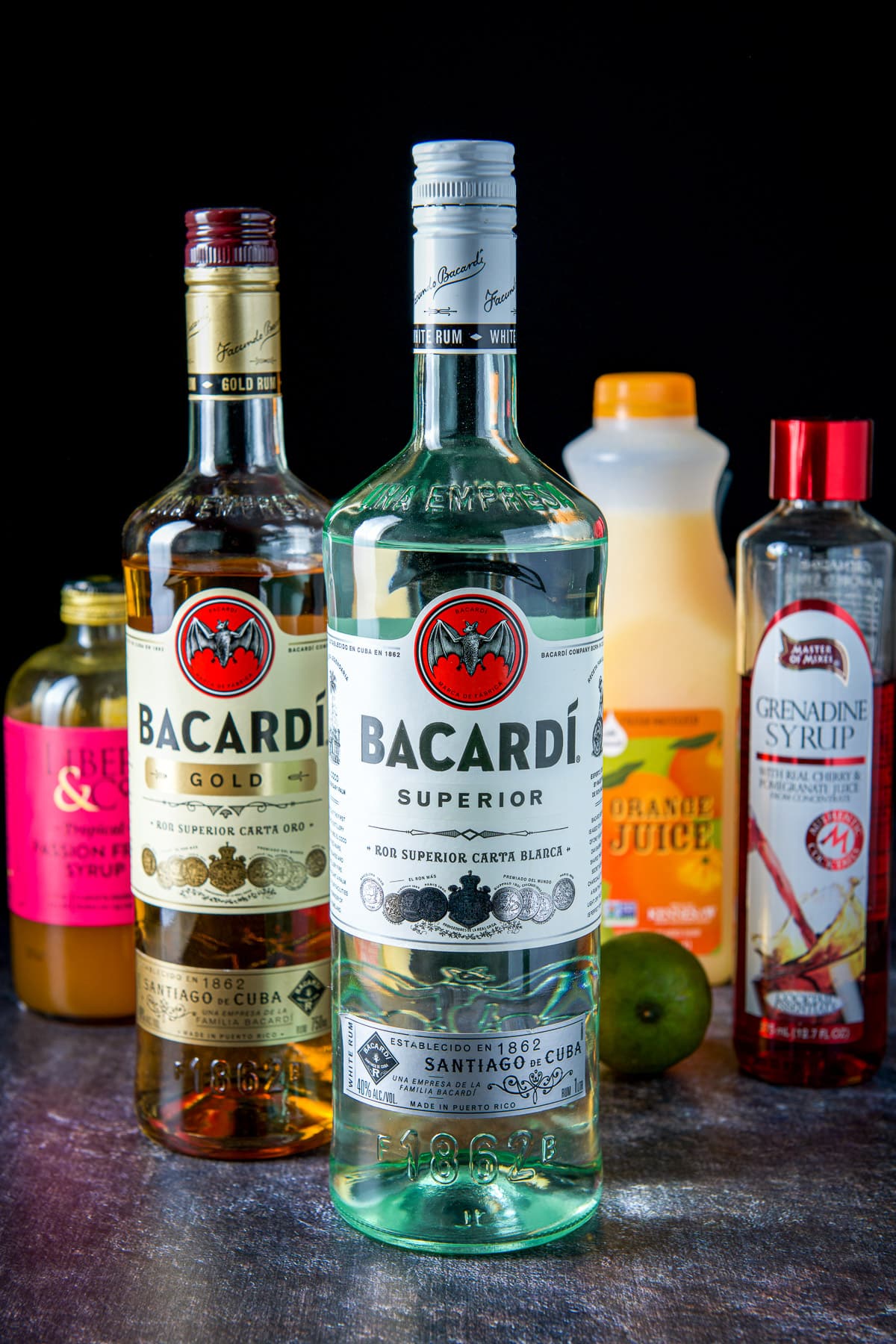 White and gold rum, orange juice, passion fruit syrup and lime on a table