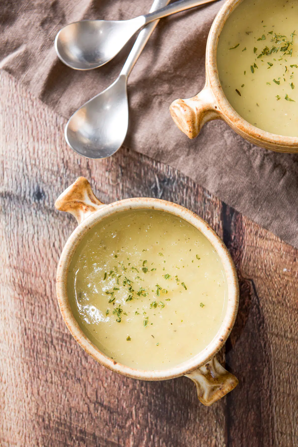 Overhead view of two crocks of leek soup with a napkin and 2 spoons