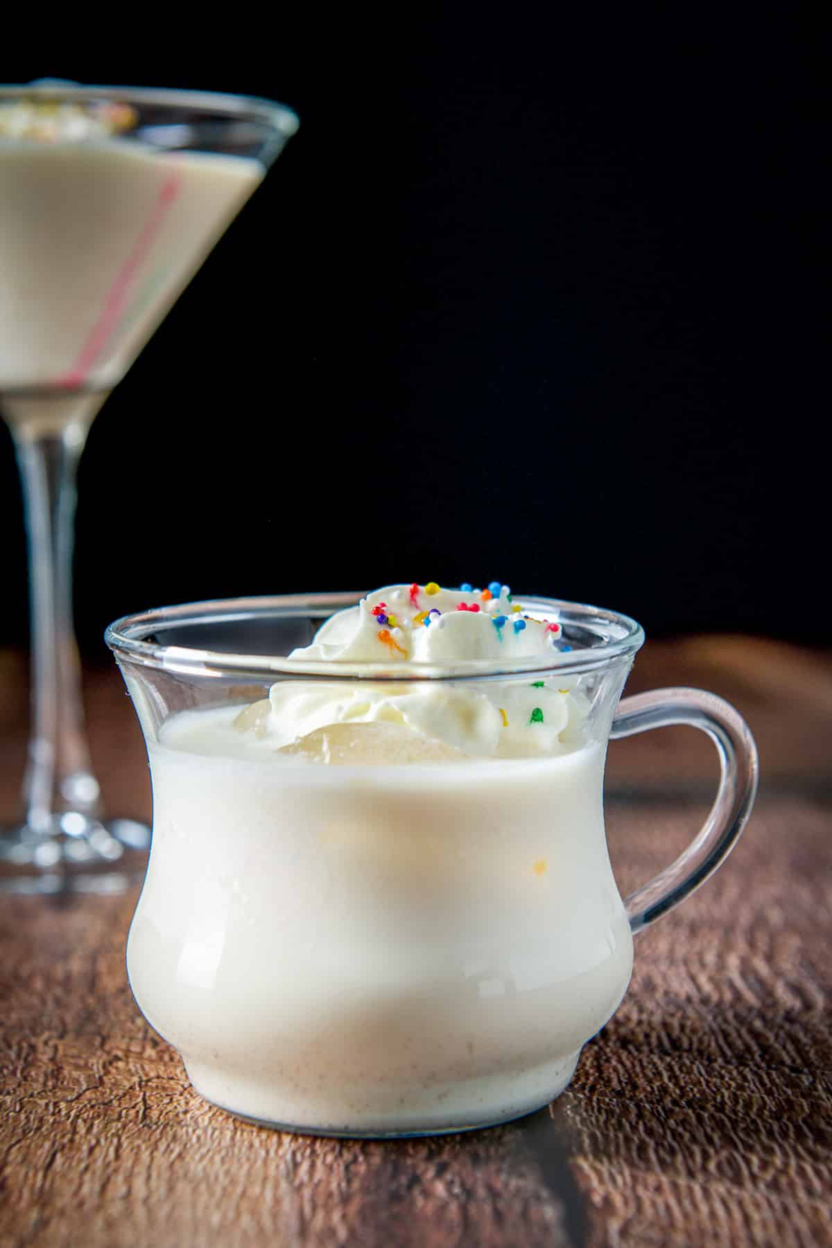 vertical view with the egg nog drink with whipped cream and colored sprinkles